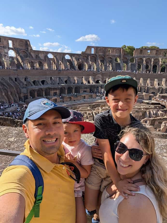 A smiling family poses for a selfie inside the Colosseum on a sunny day, capturing a memorable moment from their Rome with Kids adventure.