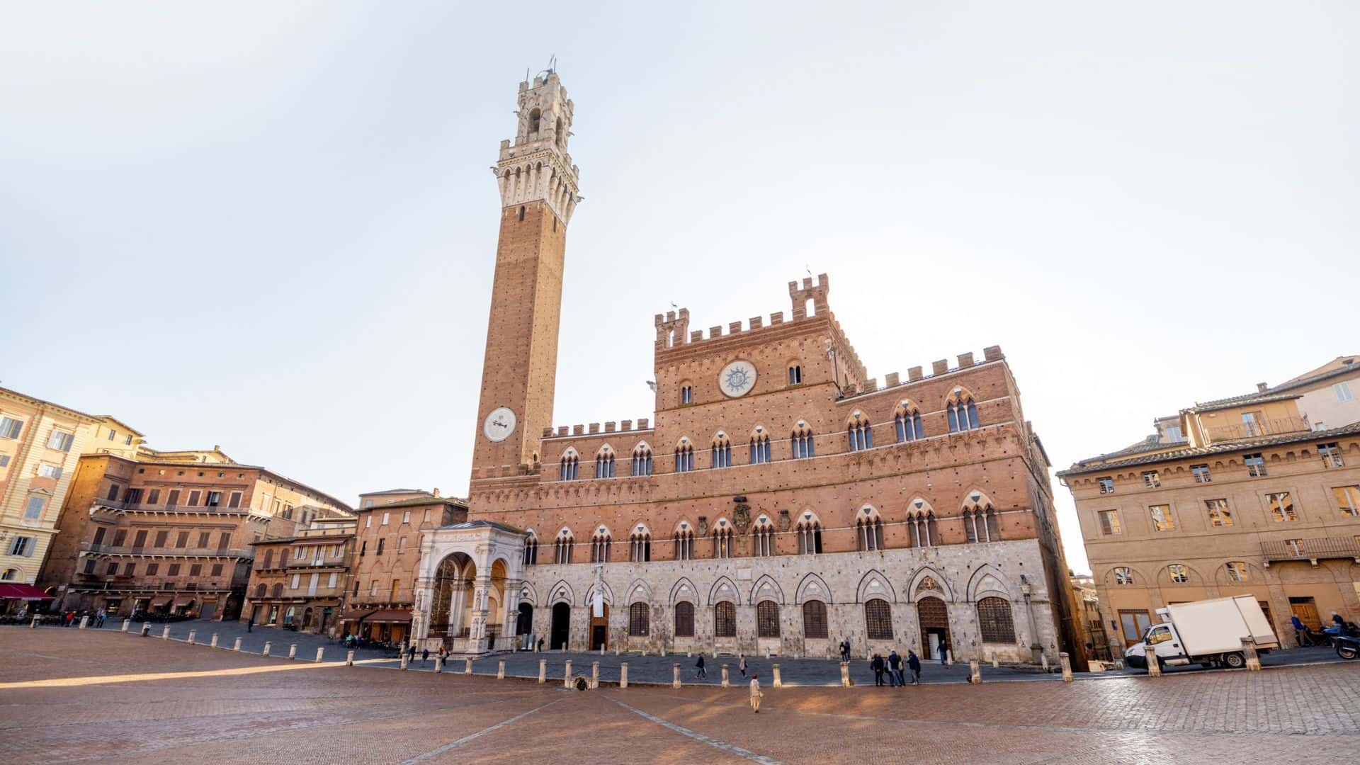 Medieval Palazzo Pubblico with tall clock tower on Siena’s Piazza del Campo, Italy, under a clear sky.
