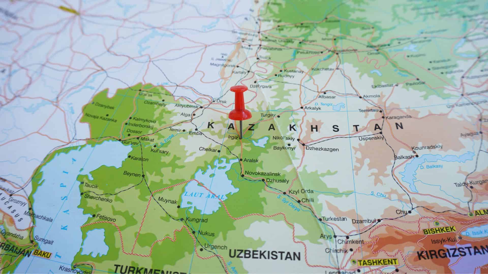 A red pushpin marks Kazakhstan on a colorful map showing surrounding countries and major cities.
