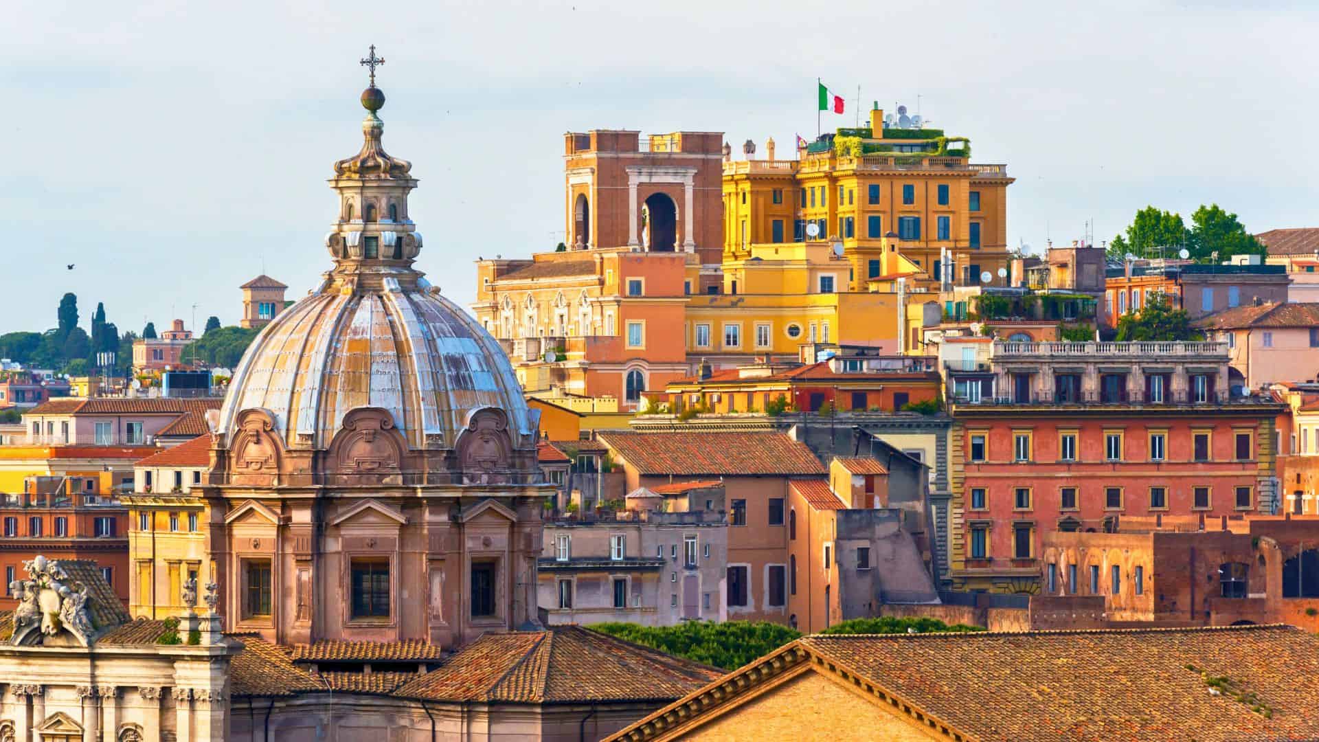 Colorful historic buildings and domes in Rome, Italy, with the Italian flag visible atop one building.