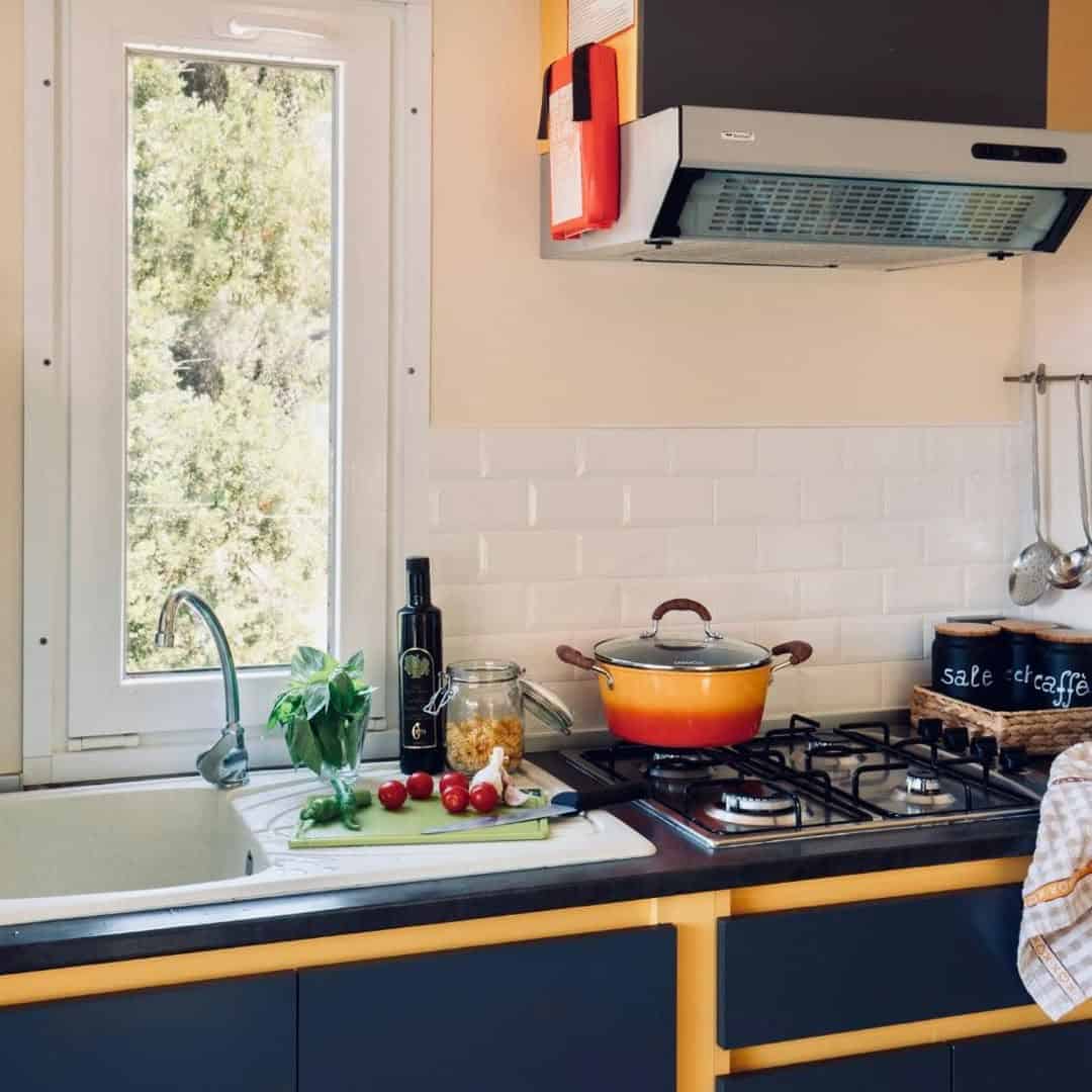 Modern kitchen with a yellow pot on the stove, fresh vegetables by the sink, and sunlight streaming in&mdash;bringing a touch of Parco della Gallinara&rsquo;s natural charm indoors.