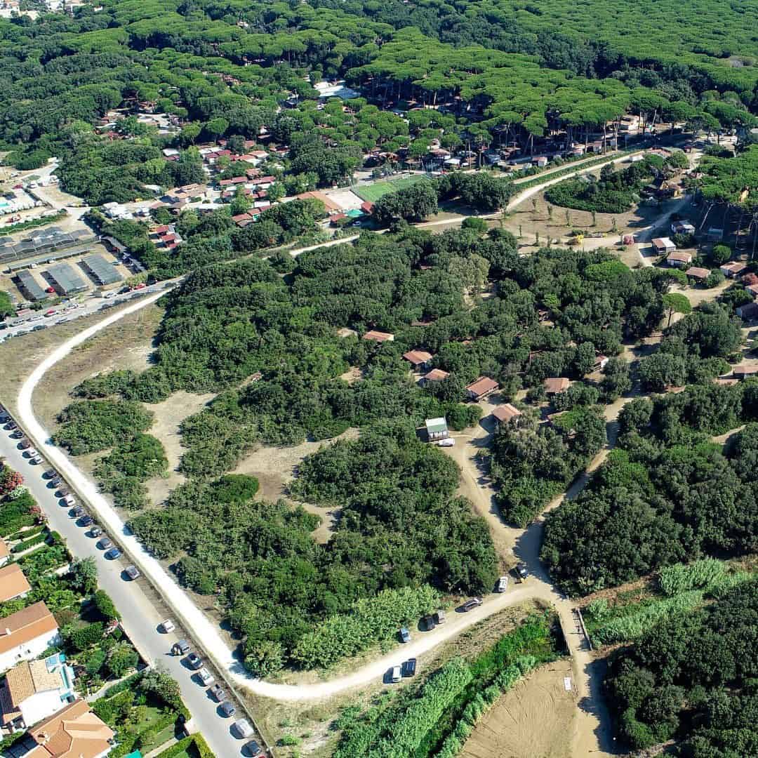 Aerial view of a neighborhood near Parco della Gallinara, with houses nestled among dense green trees and winding roads.