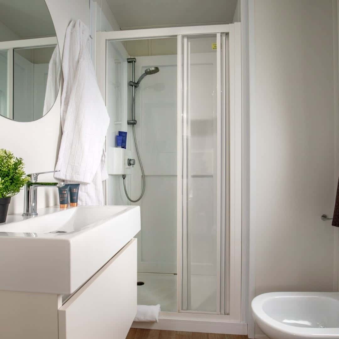 Modern bathroom with a glass shower, white sink, mirror, robe, plant, and part of a bidet visible&mdash;just steps away from Parco della Gallinara.