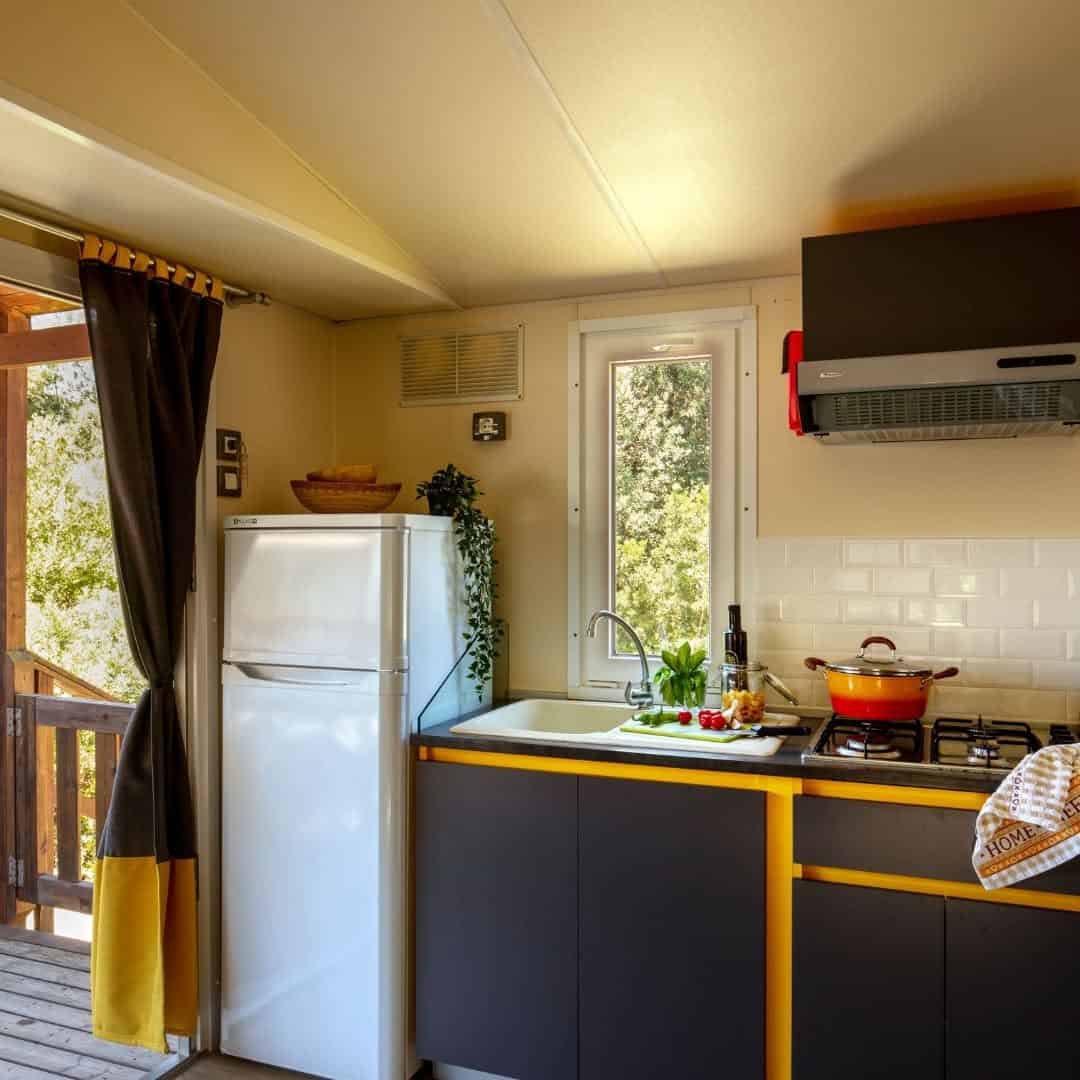 Modern kitchen with a fridge, sink, stove, cookware, and fresh vegetables near a window offering views toward Parco della Gallinara.