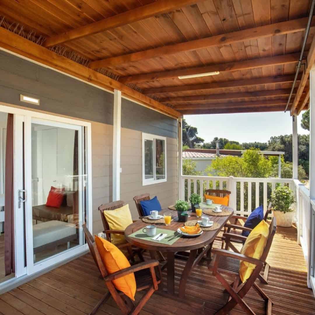 A wooden patio with a table set for breakfast, surrounded by chairs with colorful cushions, offers a peaceful retreat reminiscent of mornings at Parco della Gallinara.