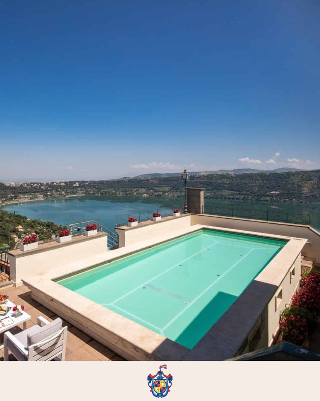 Rooftop pool overlooking a scenic lake and hills under a clear blue sky, with a dining table nearby—perfect for relaxing after exploring 4 days in Castel Gandolfo.
