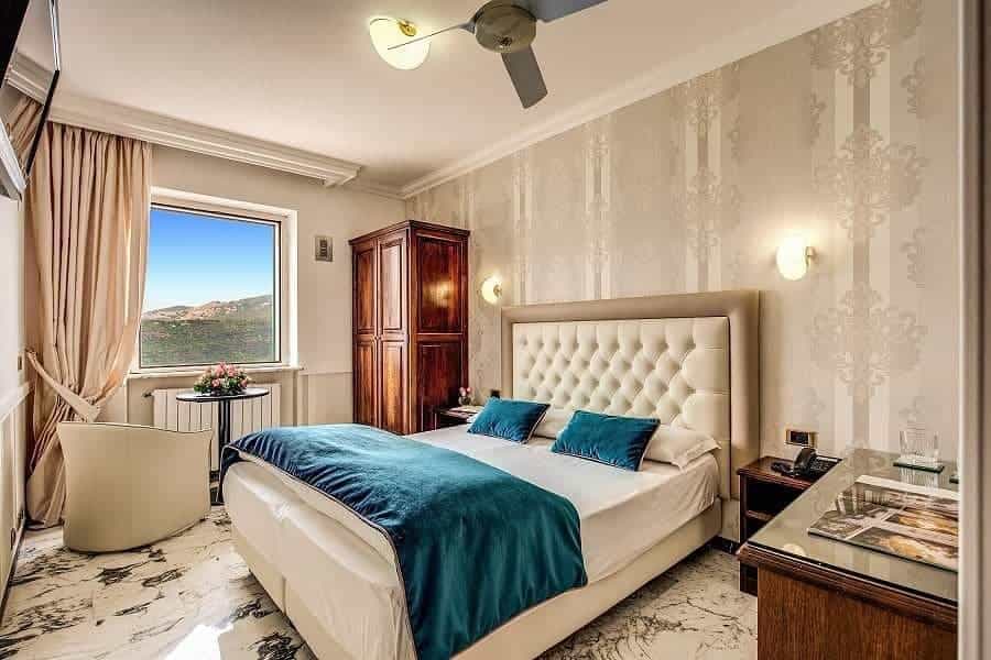 Elegant bedroom with teal accents, large window with mountain view, and modern decor—perfect for relaxing after 4 days in Castel Gandolfo.