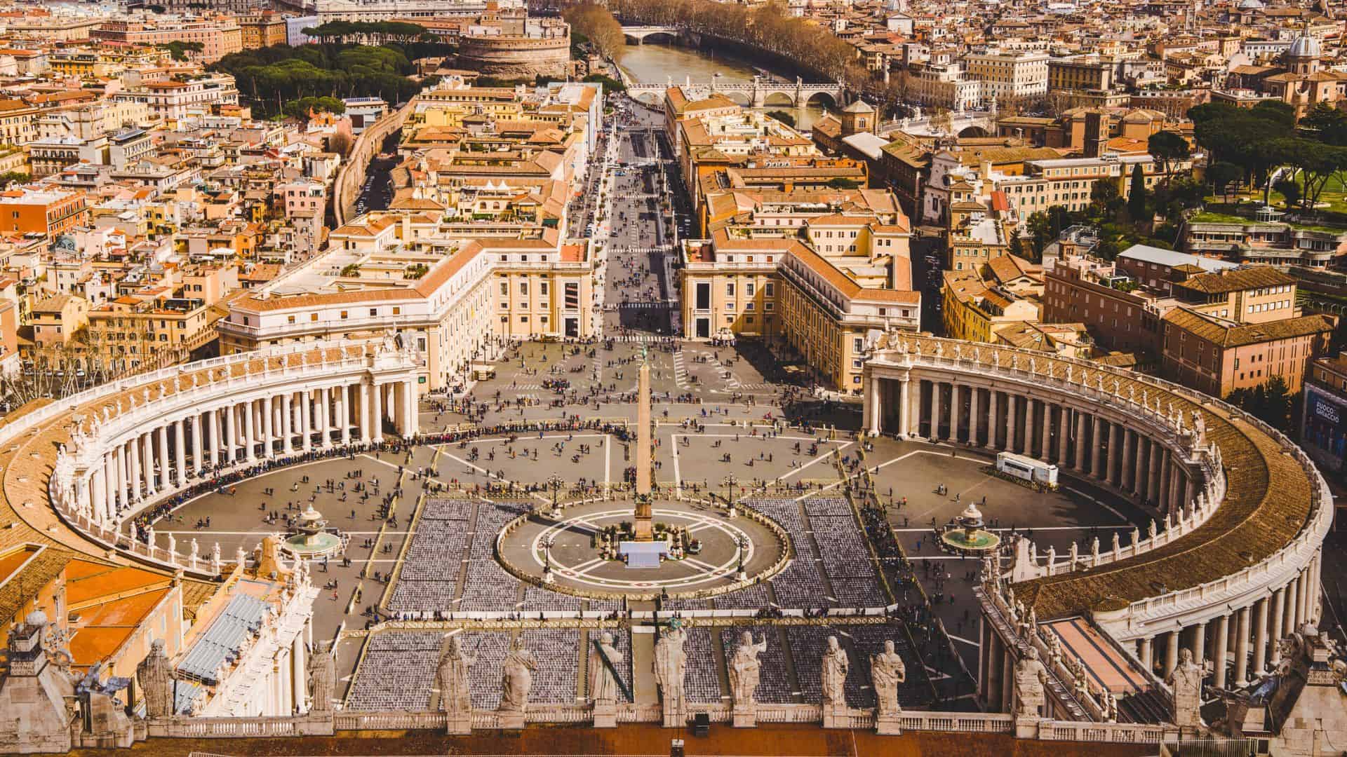 Aerial view of St. Peter’s Square in Vatican City, with crowds and surrounding historic buildings.