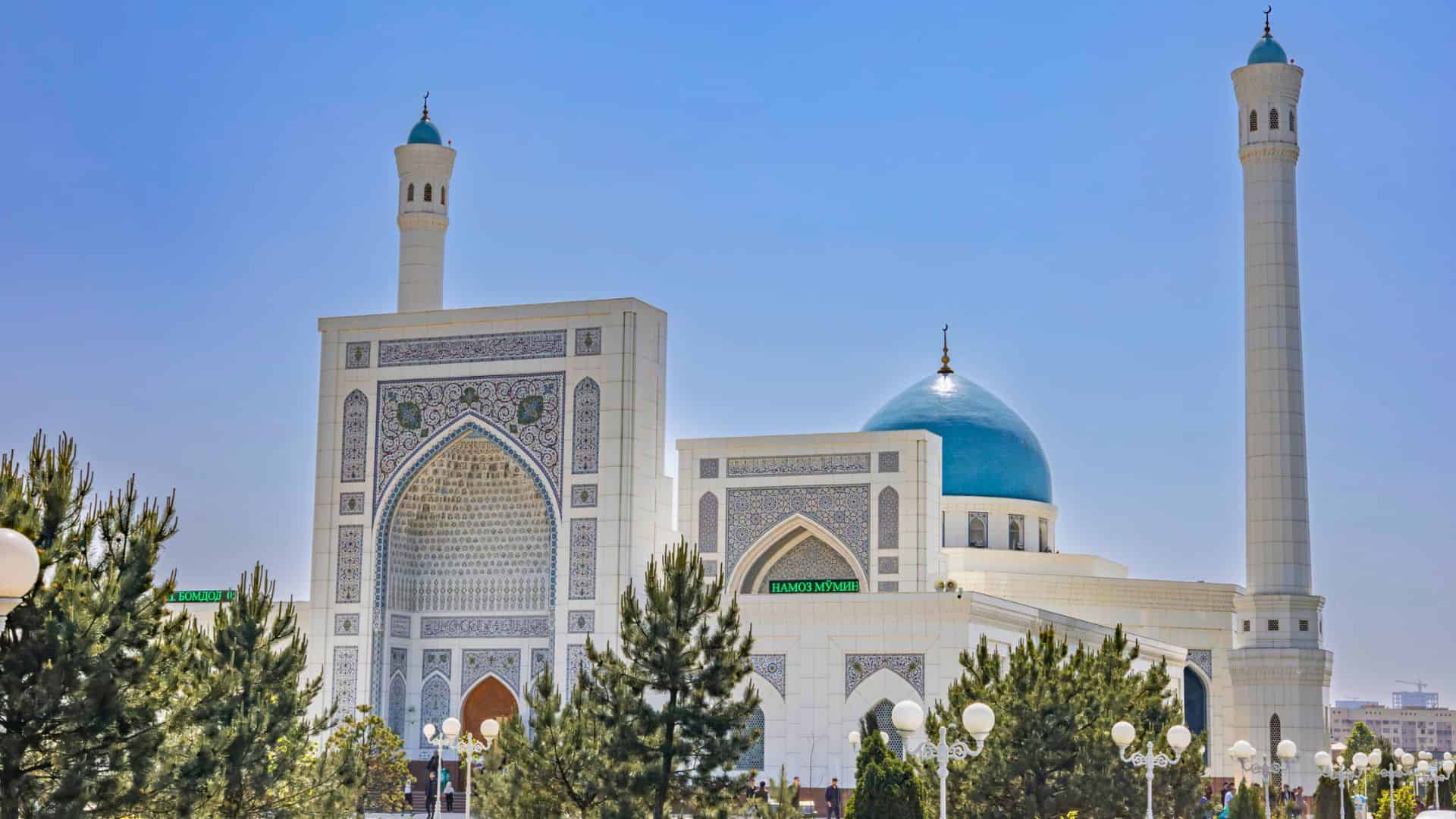 A grand mosque with a blue dome, tall minarets, and intricate tilework, surrounded by trees and lights.
