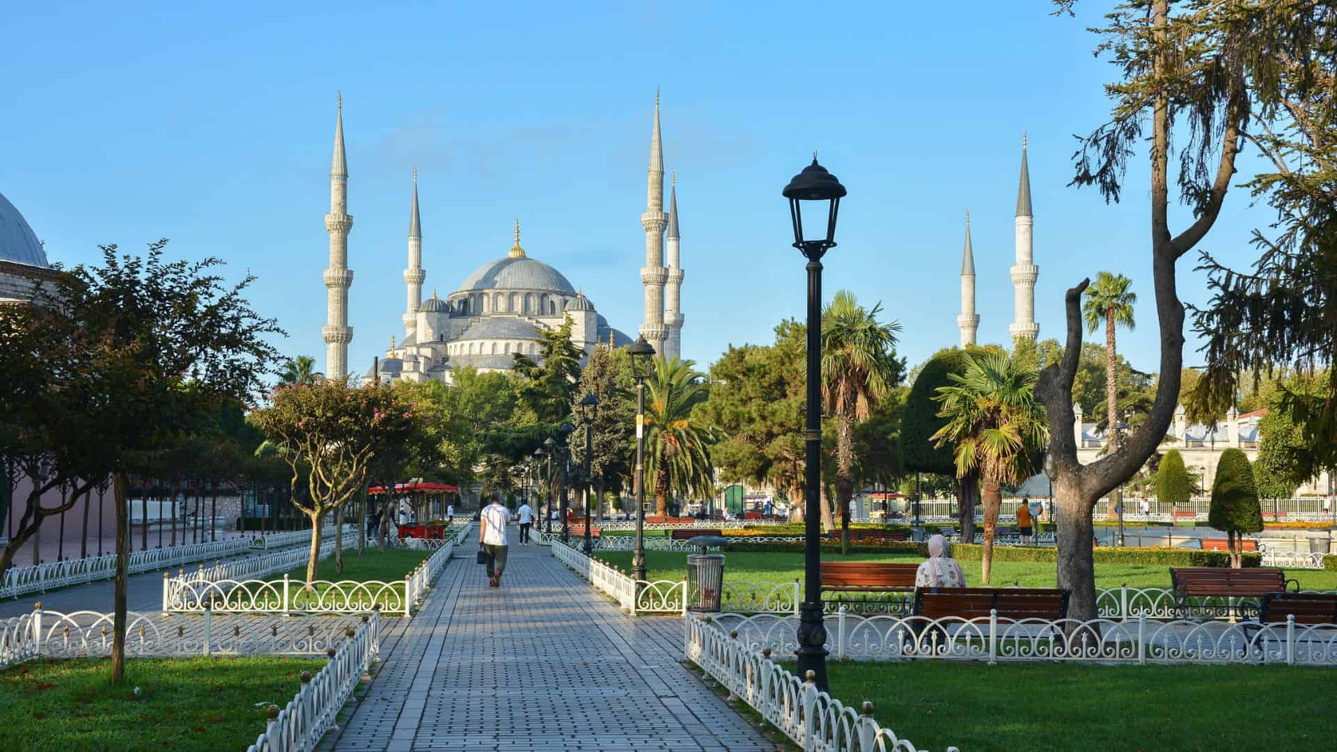 The Blue Mosque in Istanbul, with people walking and sitting in a park on a sunny day.