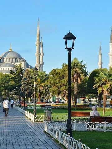The Blue Mosque in Istanbul, with people walking and sitting in a park on a sunny day.