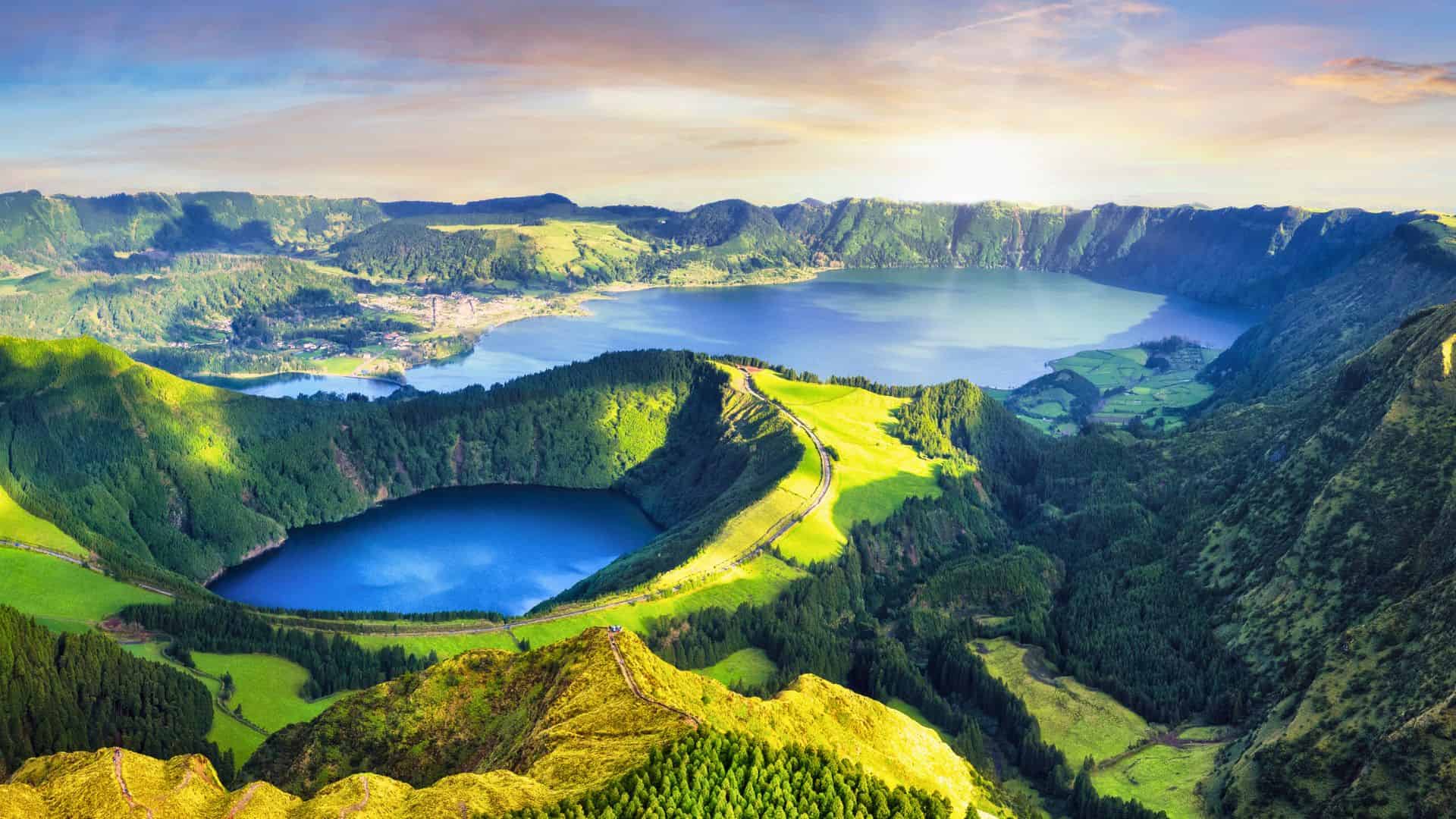 Aerial view of lush green hills and two crater lakes under a bright sky at sunrise or sunset.