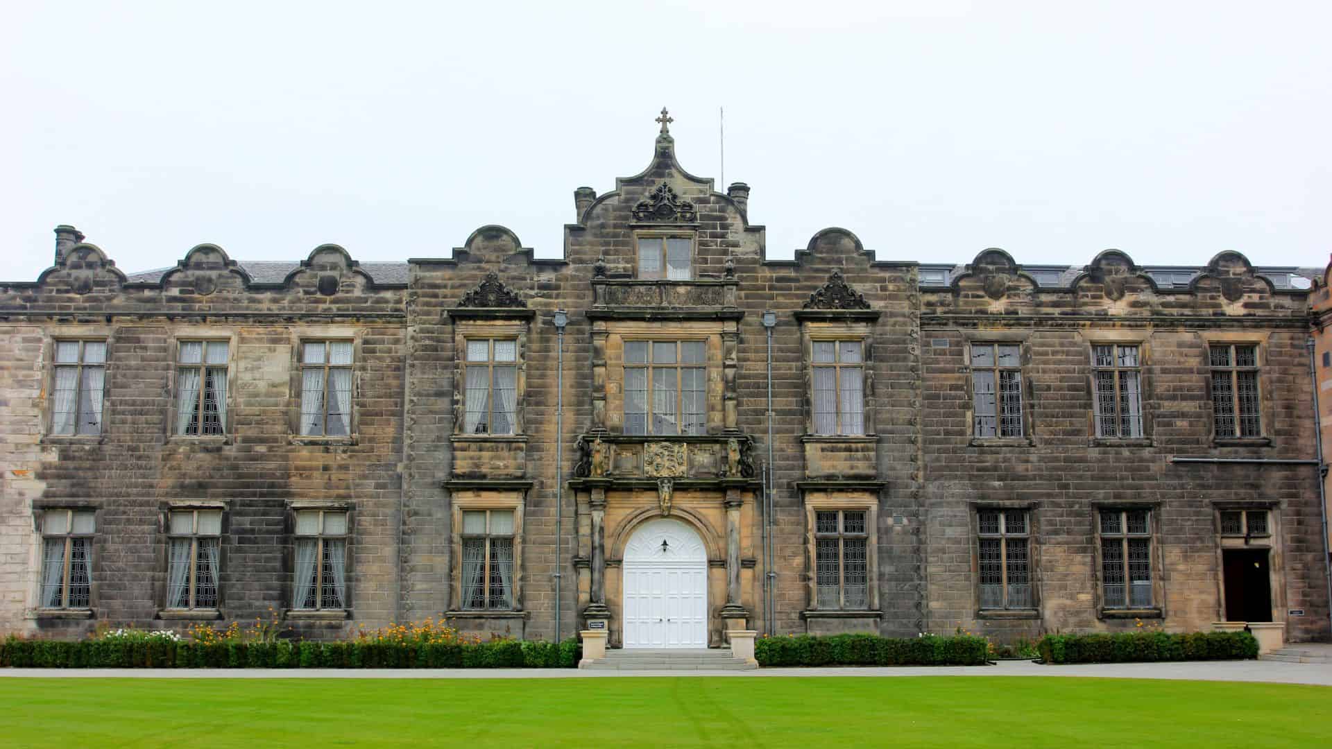 Historic stone university building with arched central doorway and neatly trimmed lawn in front.