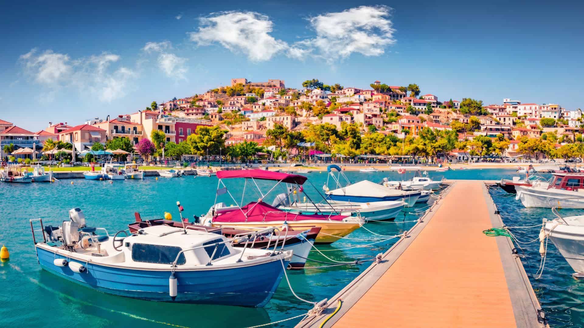 Colorful boats docked in a marina with a hillside town and blue sky in the background.