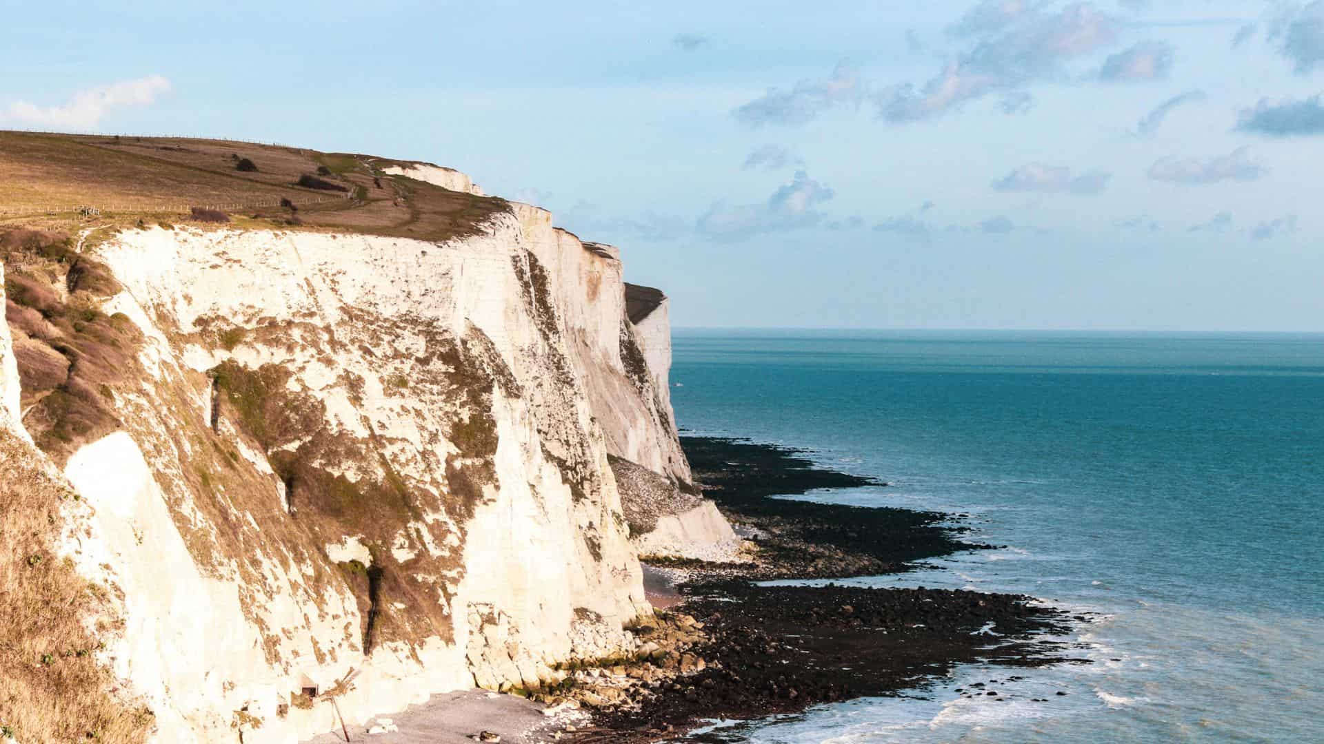 White chalk cliffs overlooking the blue sea under a partly cloudy sky.