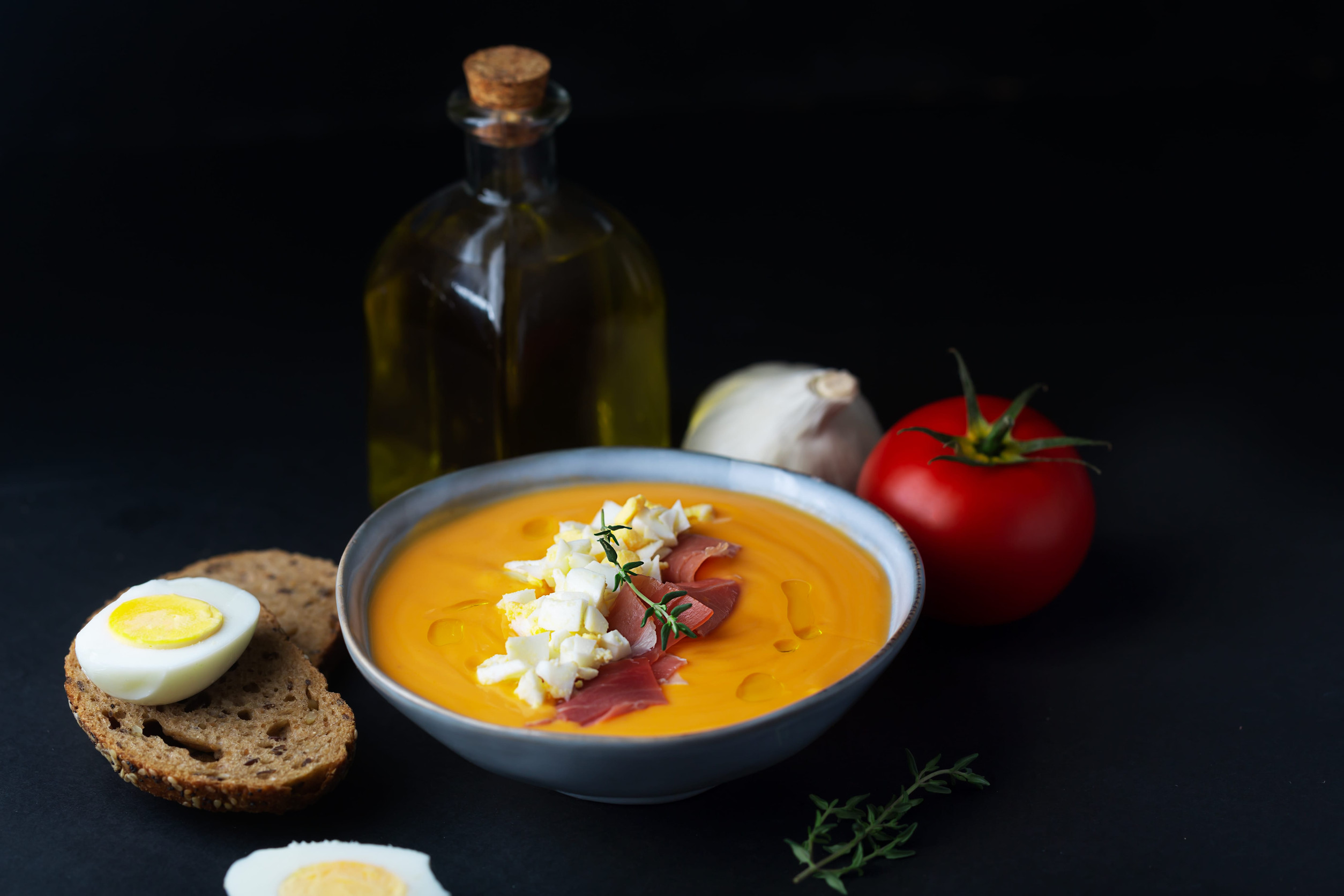 A bowl of orange soup with toppings, next to bread, boiled egg, tomato, garlic, and olive oil&mdash;a classic taste of Spain and a must-try for anyone exploring Top 10 Vegetarian Food dishes.