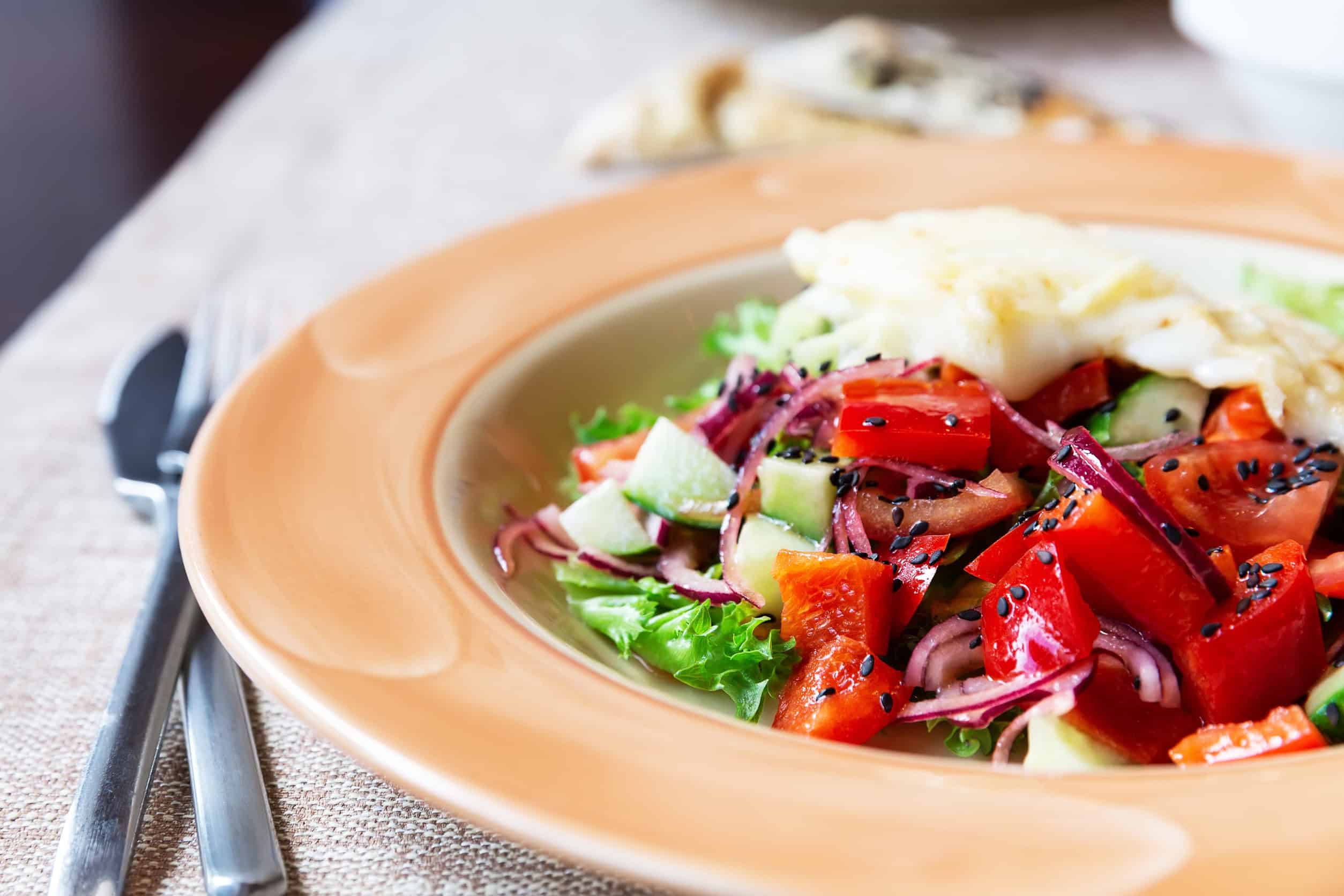 A fresh salad with lettuce, tomatoes, cucumbers, onions, and sesame seeds on an orange plate—a delightful example of Vegetarian Dishes in Tunisia.