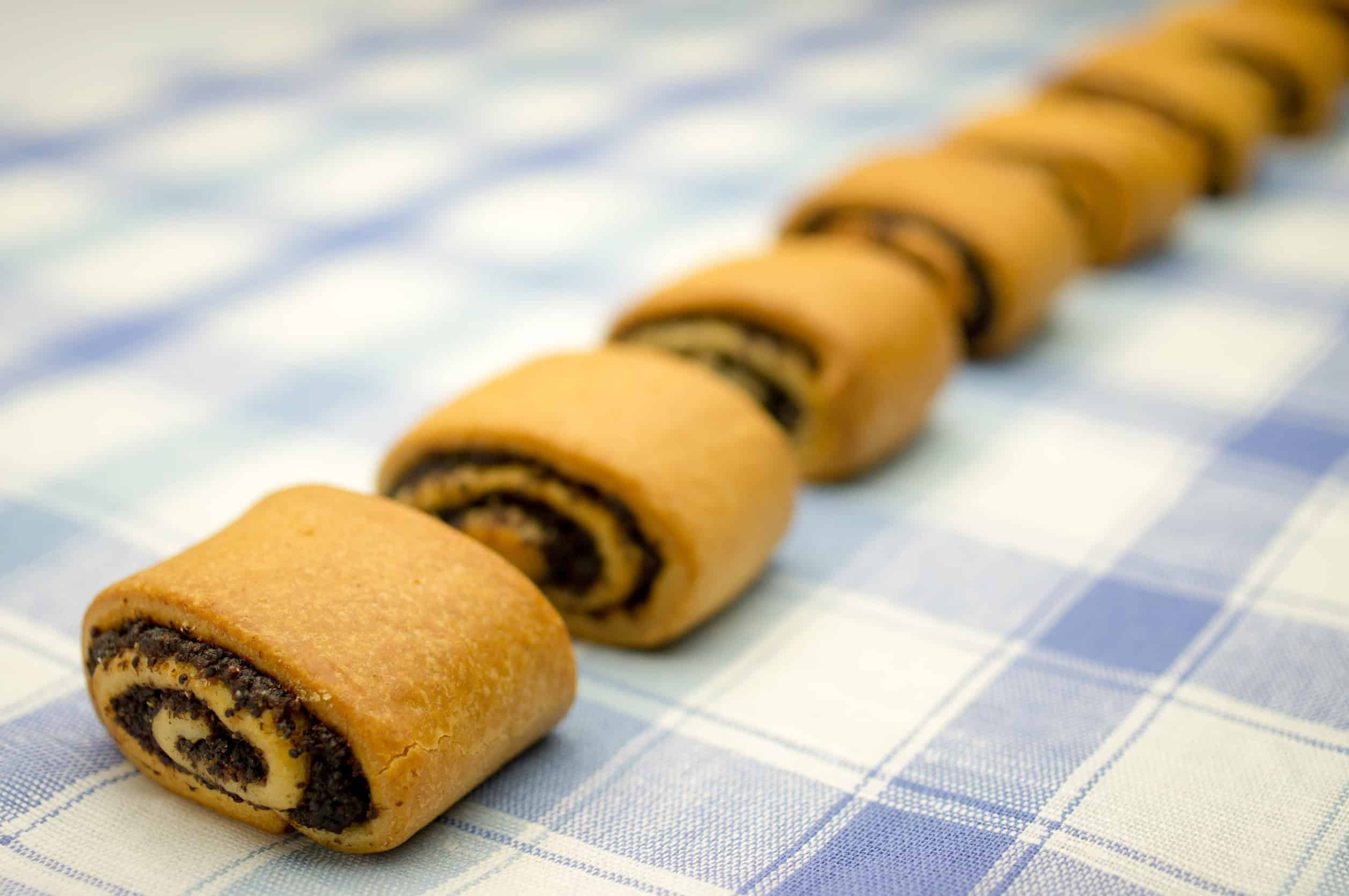 Nine pieces of rolled pastry with a dark filling, reminiscent of Vegetarian Dishes in Tunisia, are lined up on a blue and white checkered cloth.