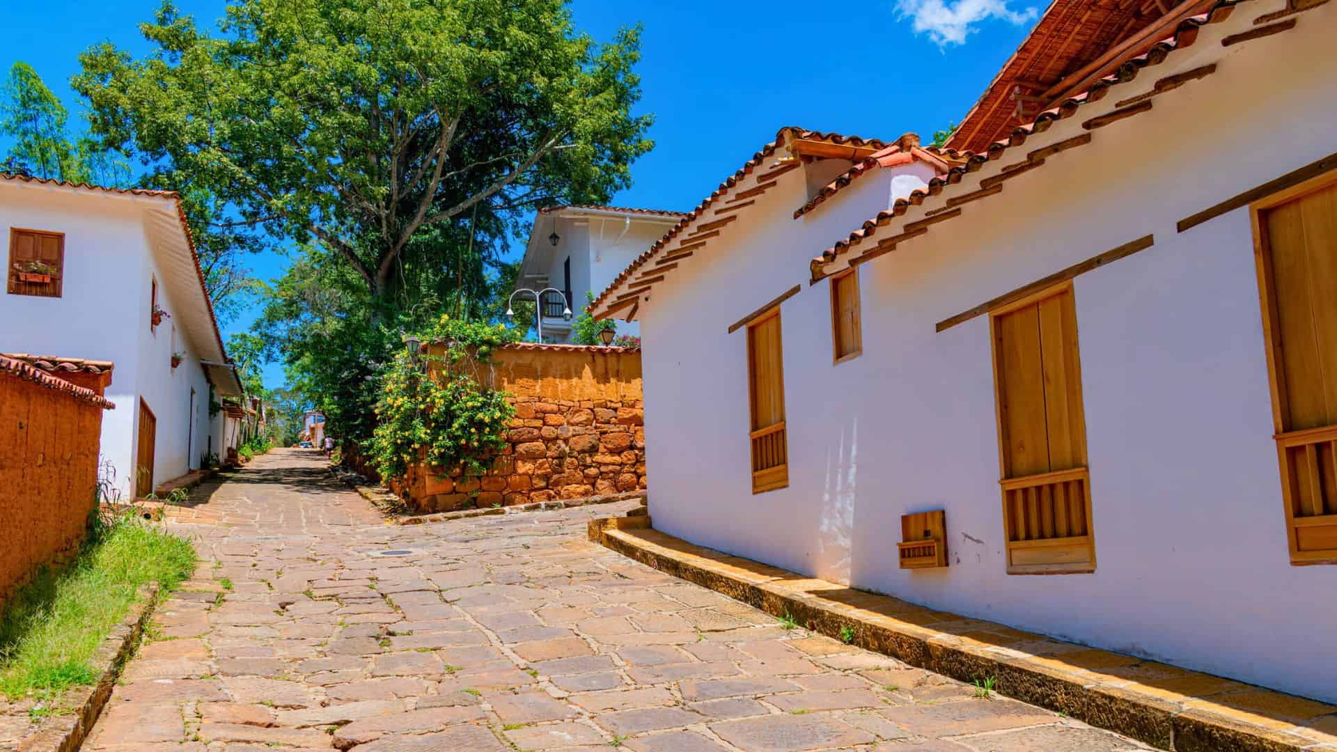 A cobblestone street lined with white houses and wooden doors under a bright blue sky.