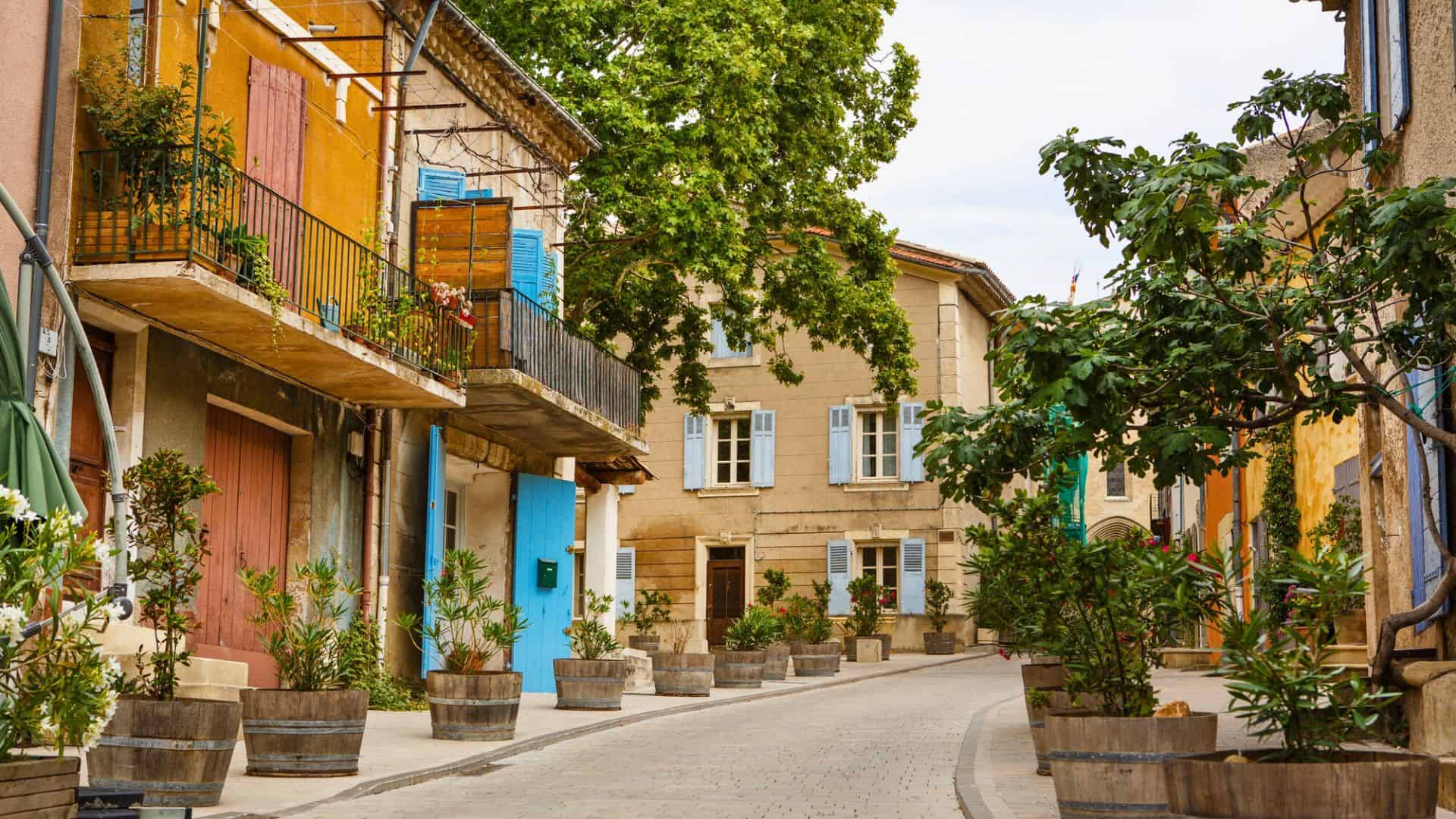 Colorful, narrow street in a European village lined with potted plants and charming buildings.