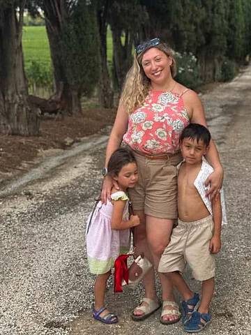 A smiling woman stands on a tree-lined path with two young children, hugging them closely—capturing the joy of one of the best day trips from Rome for families.