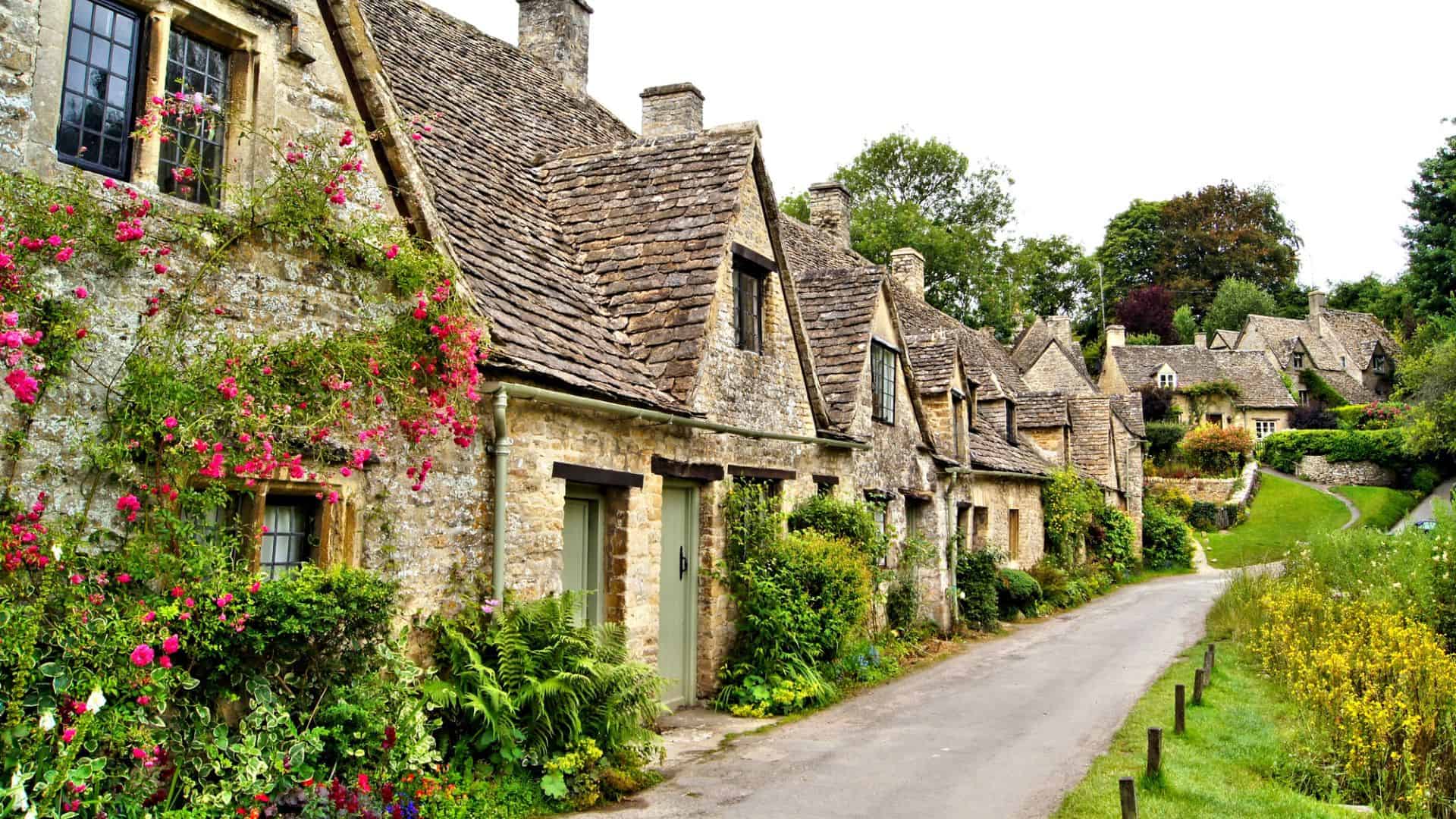 A row of quaint stone cottages with flower gardens along a narrow road in a peaceful countryside village.