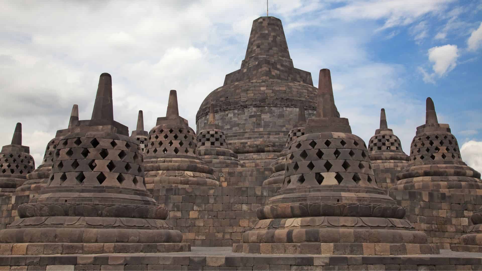 Ancient stone stupas and dome structure at Borobudur Temple in Indonesia under a cloudy sky.