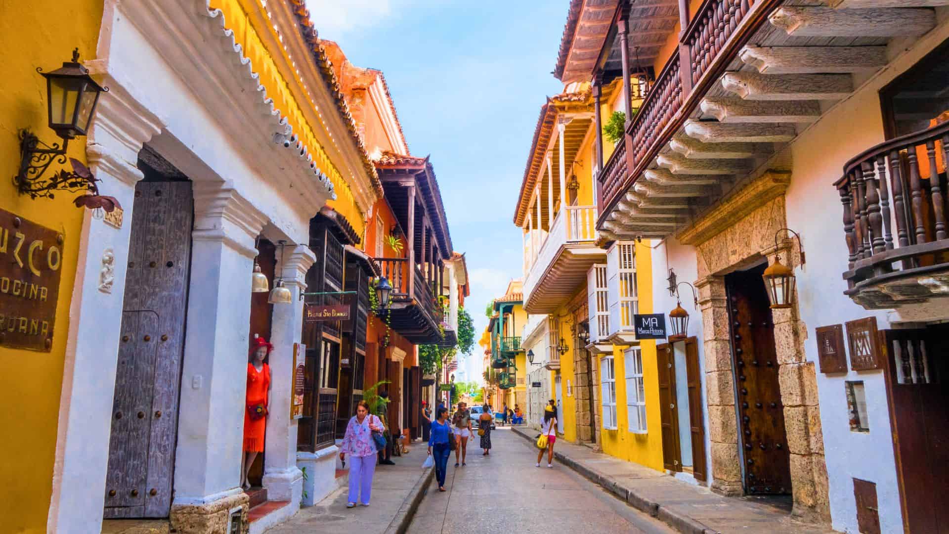 Colorful colonial buildings line a lively street with people walking in a historic city.