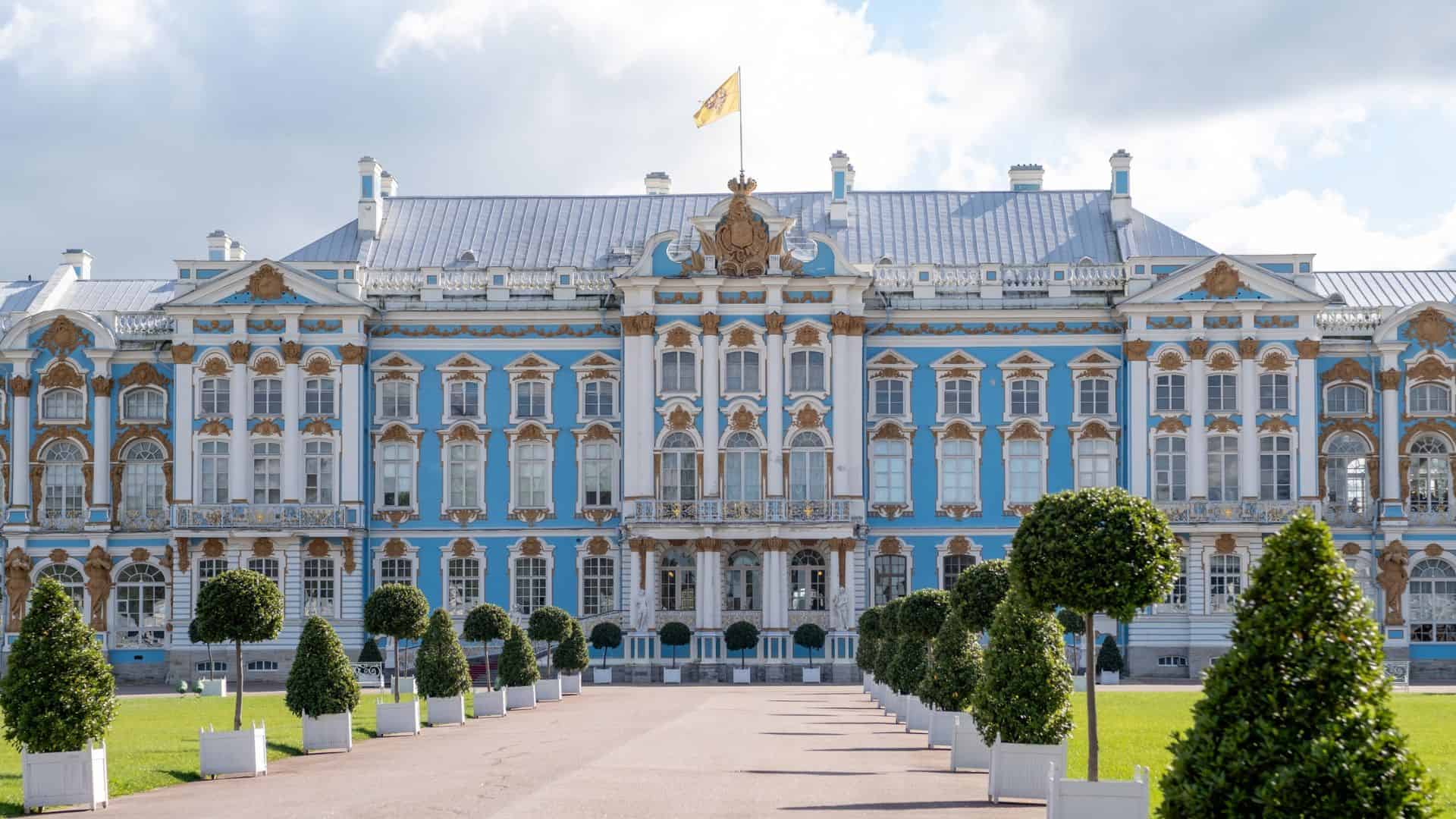 A grand blue and white palace with ornate gold details, manicured trees, and a flag on top.