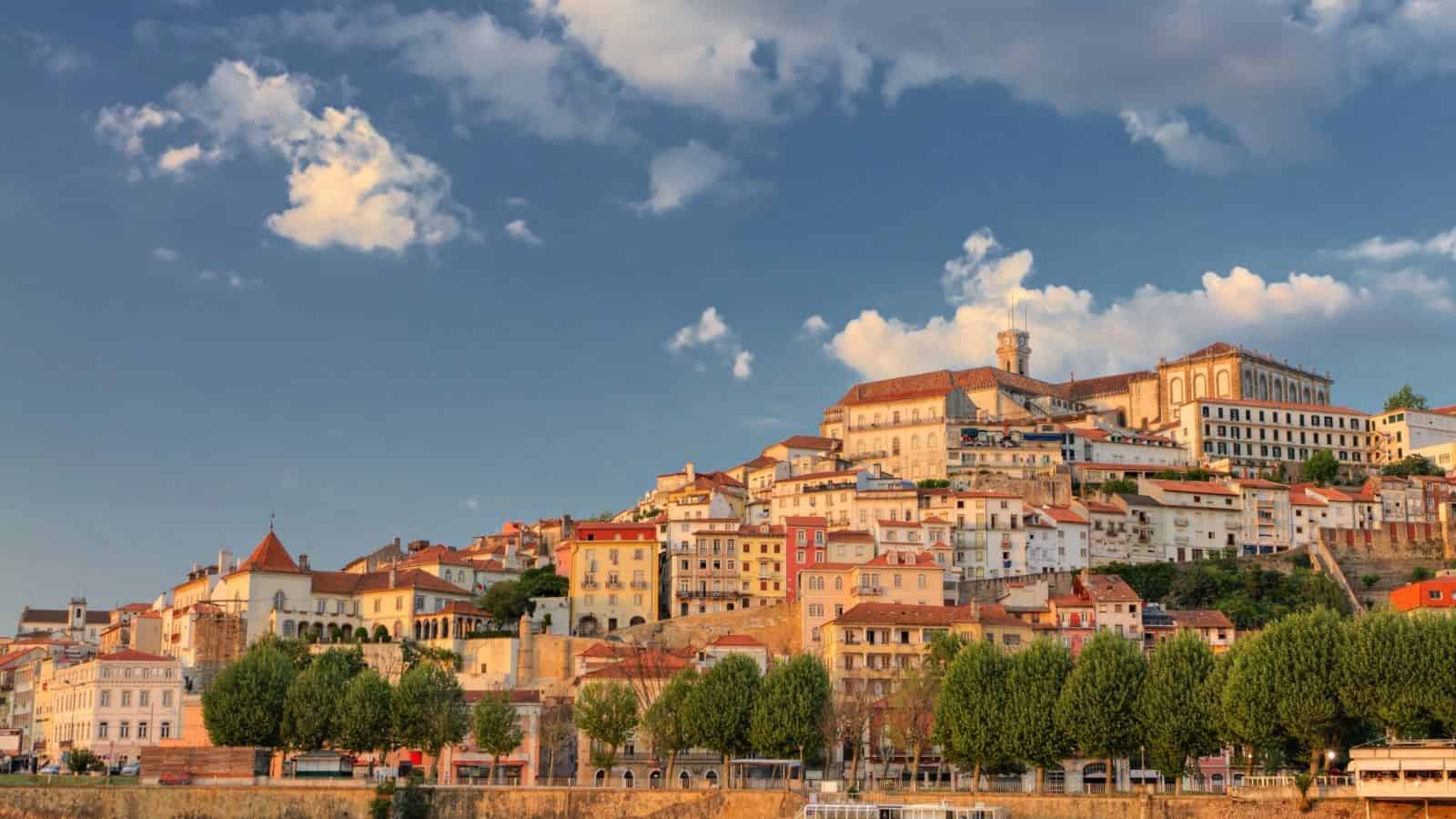 A hillside cityscape with historic buildings and trees under a blue sky with scattered clouds.