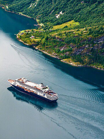 A cruise ship sails through a narrow, scenic fjord surrounded by green hills and rocky cliffs.