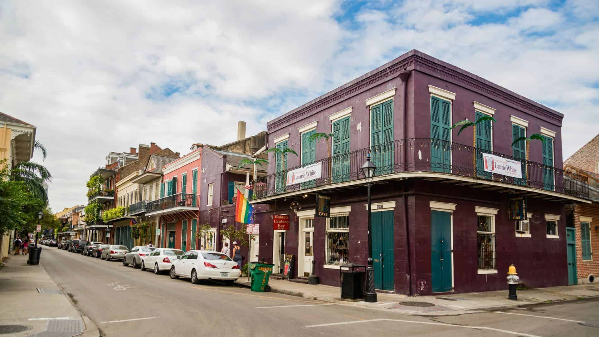 Colorful buildings with balconies line a quiet street in New Orleans’ French Quarter under a partly cloudy sky.