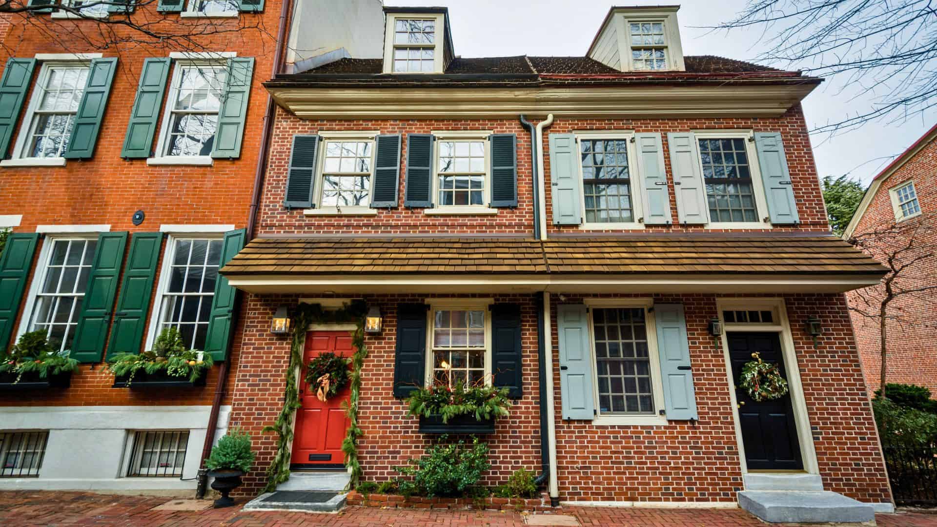 Two brick row houses with colorful shutters and holiday wreaths on the red and black front doors.