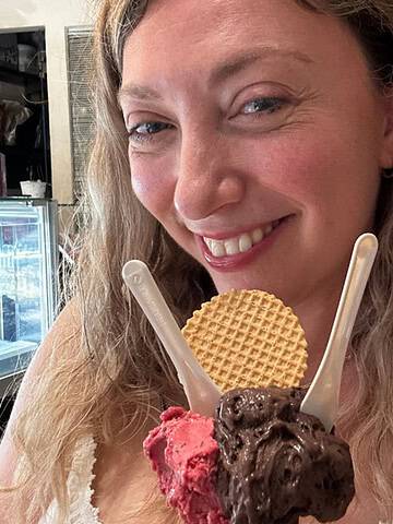Smiling woman holding gelato with chocolate, berry flavors, two spoons, and a round wafer—perfect after exploring Gluten Free Restaurants in Rome.