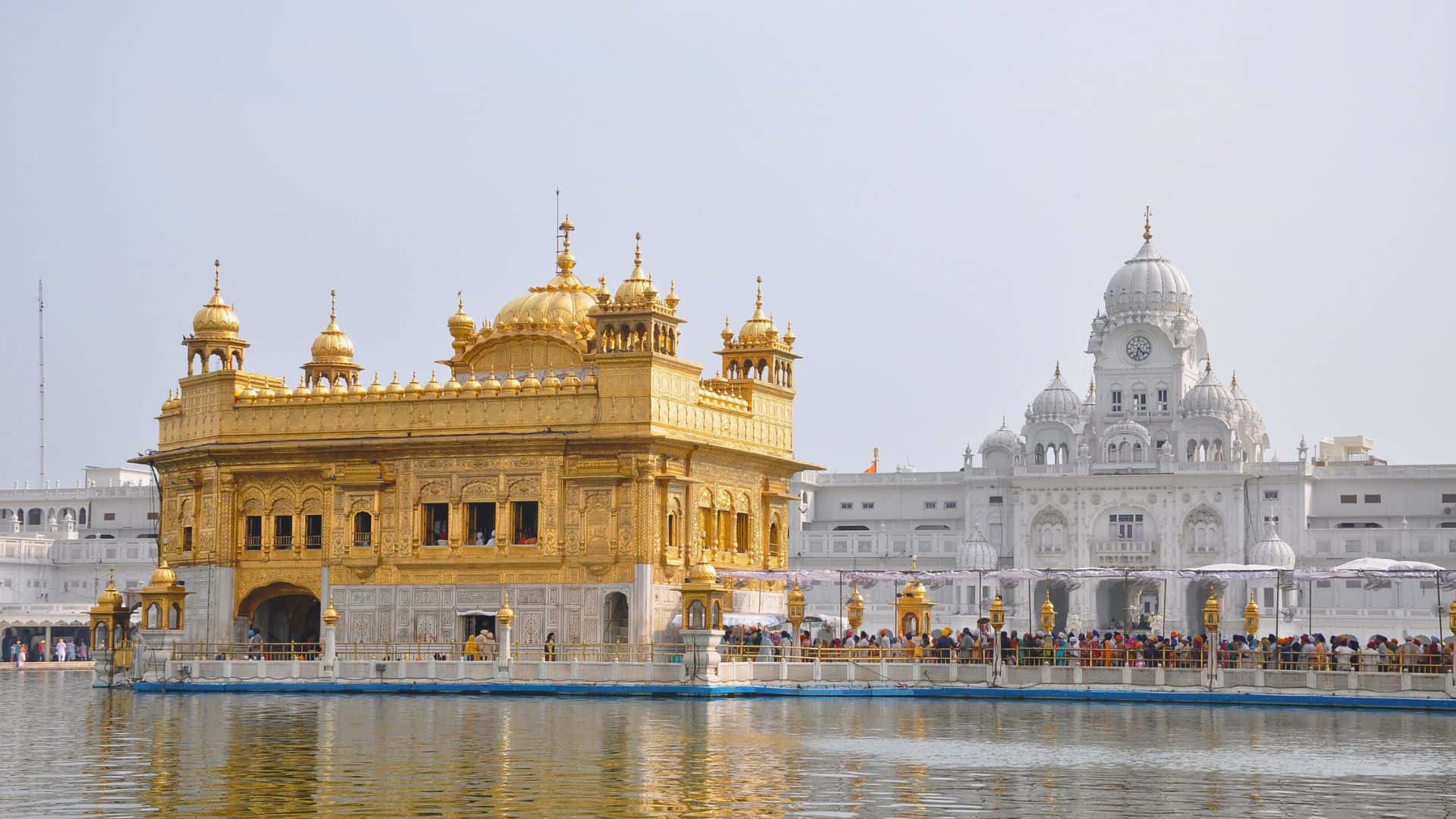 Golden Temple in Amritsar, India, with its golden facade and reflection in the surrounding water, under a clear sky.