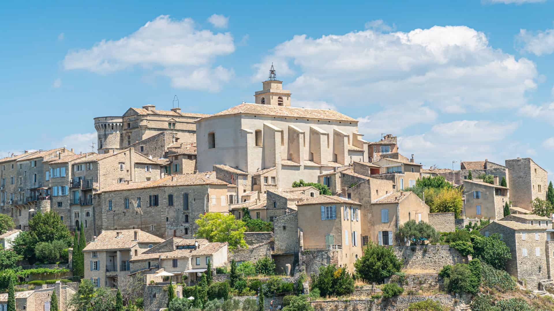 Hillside village with stone buildings and a large church under a blue sky with scattered clouds.