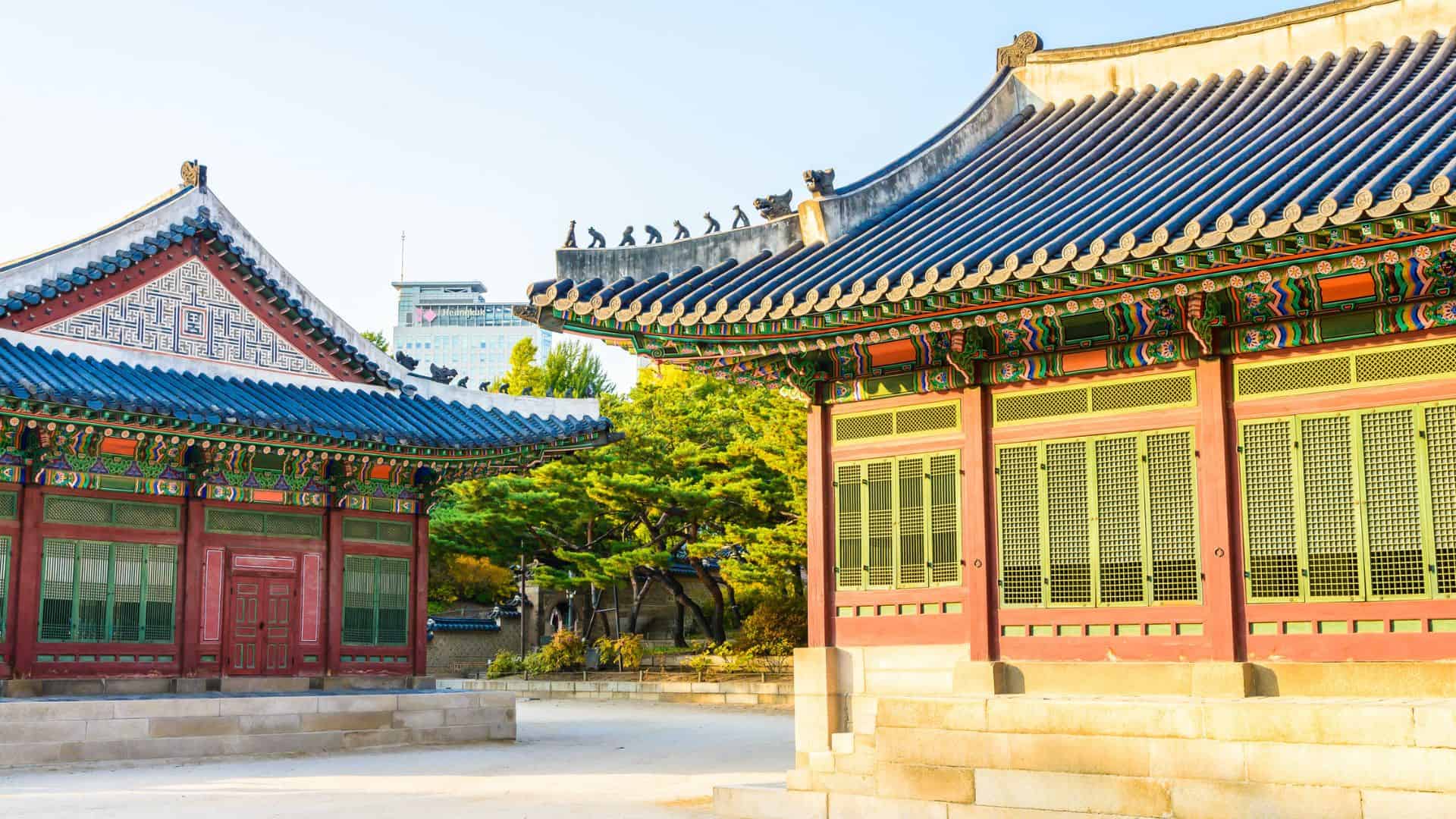 Traditional Korean palace buildings with colorful roofs and ornate details under a clear sky, surrounded by trees.