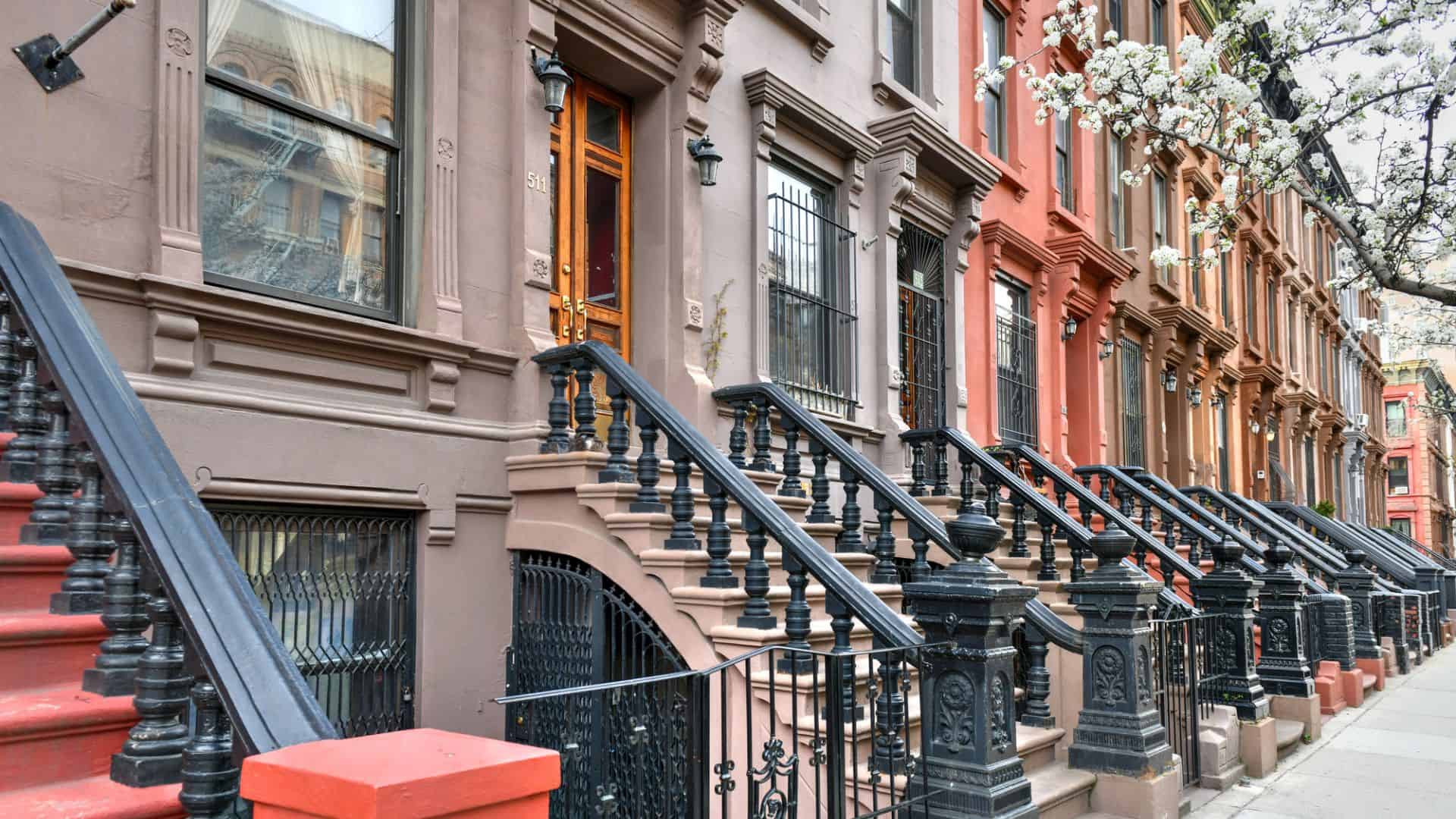 A row of colorful brownstone townhouses with stairs and iron railings on a city street.