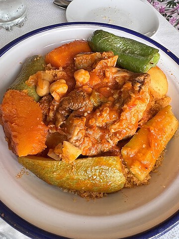 A bowl of couscous topped with vegetables, chickpeas, and meat in a red sauce—a classic dish often featured alongside Vegetarian Dishes in Tunisia.