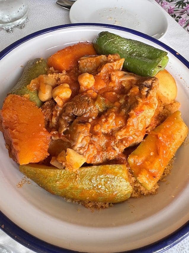 A bowl of couscous topped with vegetables, chickpeas, and meat in a red sauce—a classic dish often featured alongside Vegetarian Dishes in Tunisia.