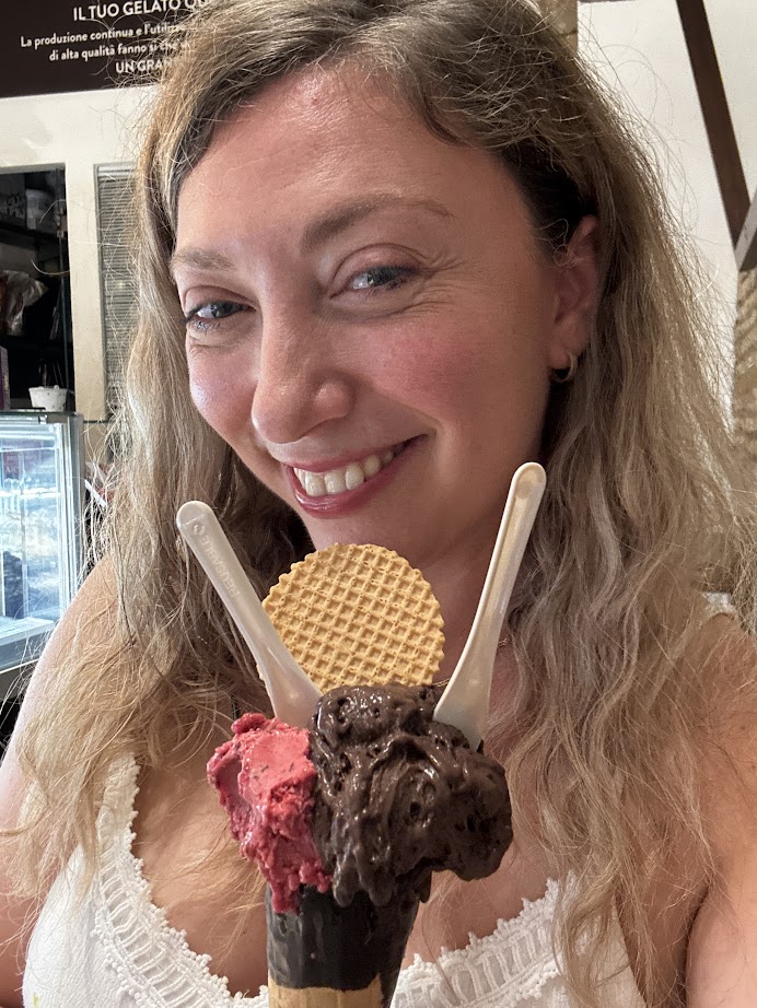 Smiling woman holding an ice cream cone with chocolate, berry scoops, wafer, and two spoons—just steps away from some of the best gluten free restaurants in Rome.