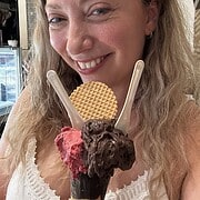 Smiling woman holding an ice cream cone with two flavors, two spoons, and a wafer on top—perfect for anyone exploring Gluten Free Restaurants in Rome.