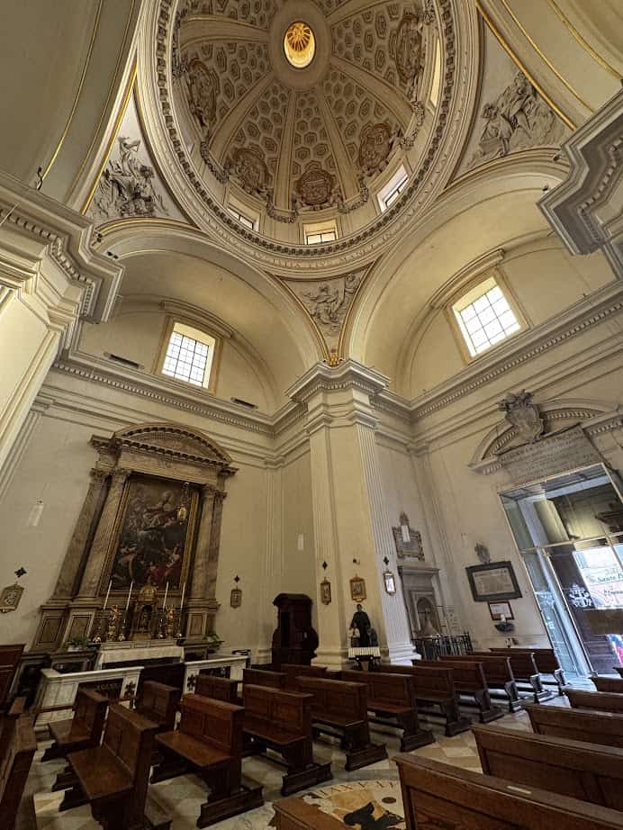 Interior of a church in Castel Gandolfo with wooden pews, an ornate dome ceiling, large windows, and religious artwork above the altar—an inspiring sight to discover during 4 days in Castel Gandolfo.