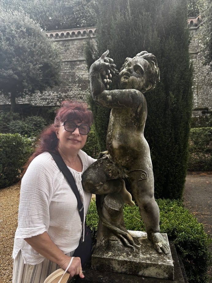 Woman in sunglasses poses beside a weathered cherub statue holding grapes in a garden setting, capturing the charm of 4 days in Castel Gandolfo.
