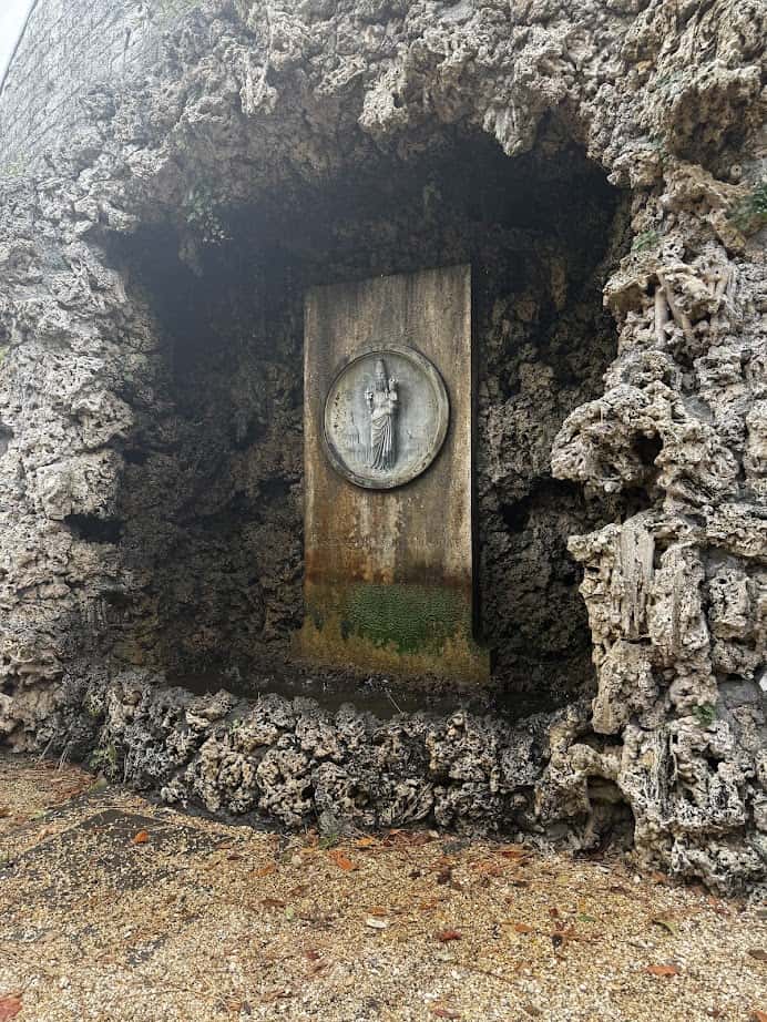 A stone grotto with a weathered round relief sculpture set in a rectangular plaque surrounded by rough rocks—an enchanting sight to discover during your 4 days in Castel Gandolfo.