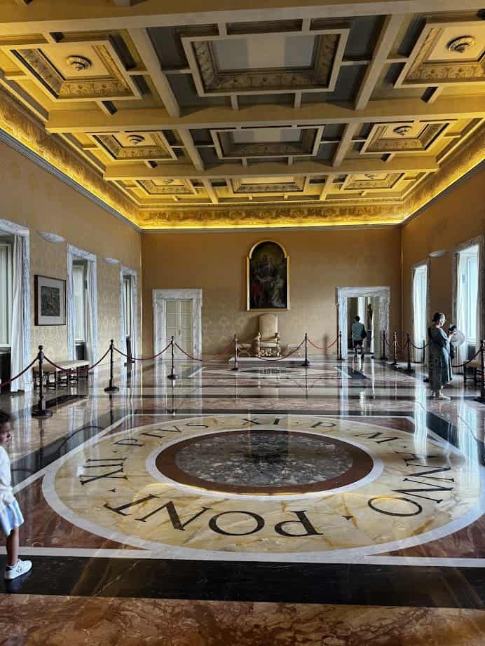 Ornate golden room with marble floor, rope barriers, artwork, and visitors taking photos during their 4 days in Castel Gandolfo.