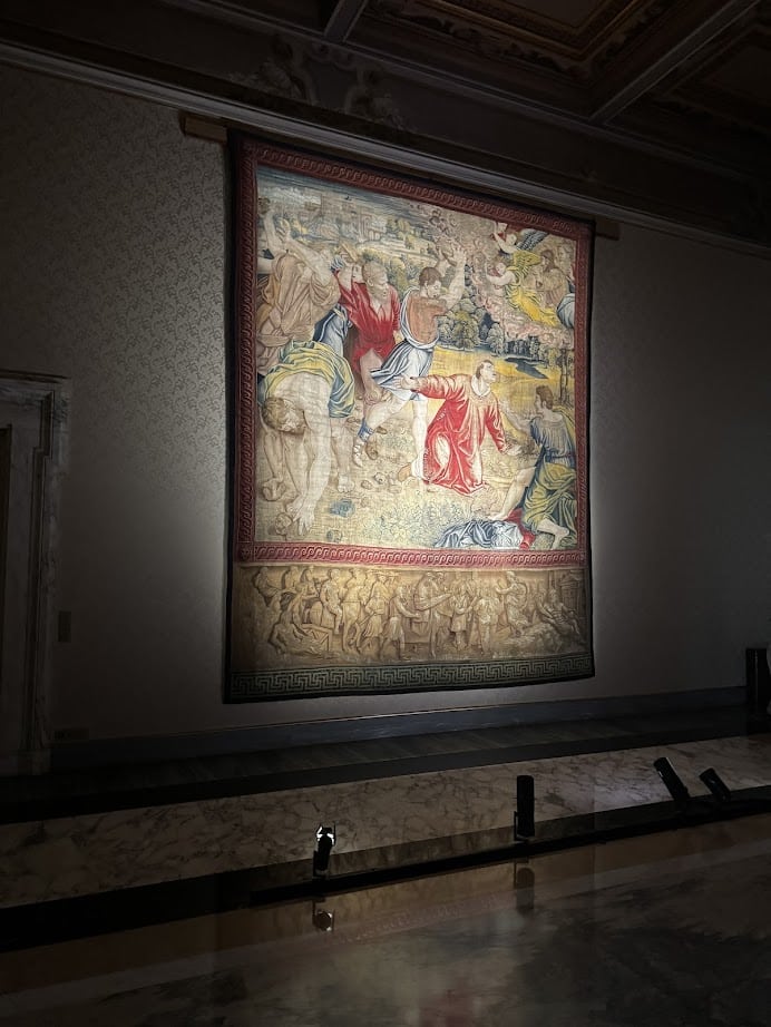 Large, ornate tapestry depicting a historical or biblical scene, reminiscent of art you might discover during 4 days in Castel Gandolfo, illuminated on a museum wall.