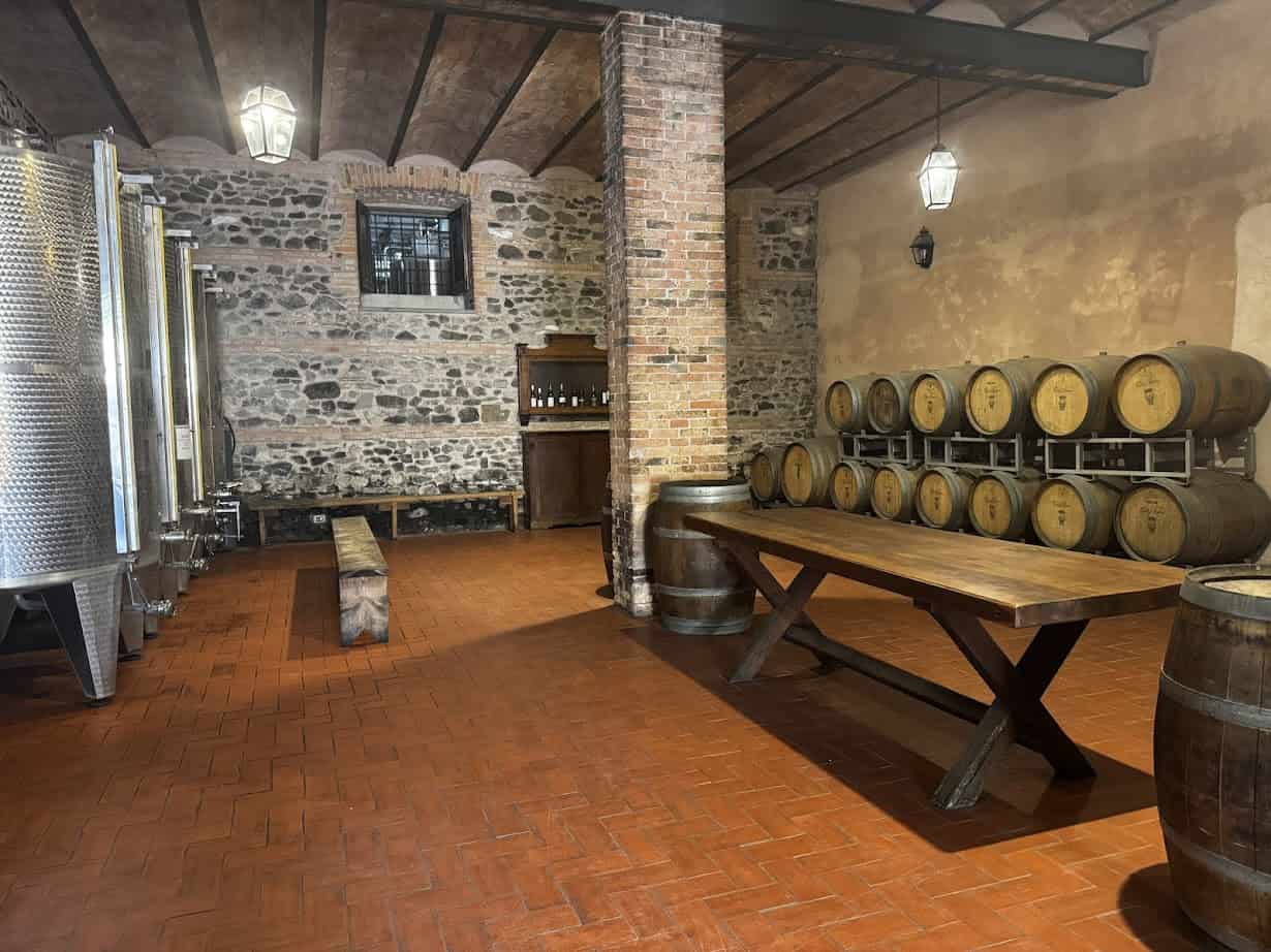 Rustic winery room with wine barrels, metal tanks, wooden table, benches, and brick walls—perfect for savoring memories of 4 days in Castel Gandolfo.