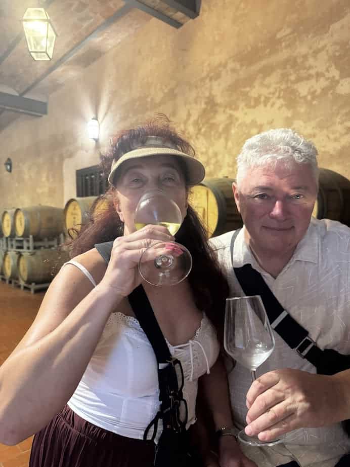 A woman and man smile while wine tasting in a cellar with barrels in the background, enjoying their 4 days in Castel Gandolfo.