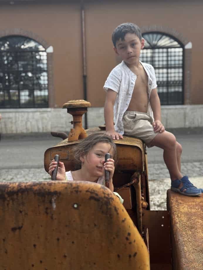 Two children play on a rusty old tractor, one sitting on top and the other pretending to drive&mdash;capturing the kind of fun you find on the best day trips from Rome for families.